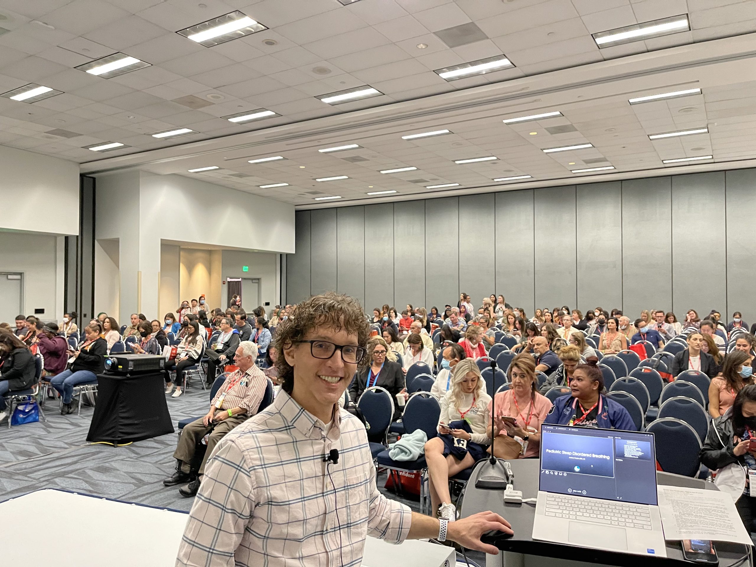 Dr Trosien facing the camera with a smile as they prepare to speak at a conference. Subject of the talk is Pediatric Sleep Disordered Breathing representing one of their many specialties.